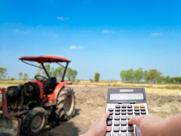 Agriculture investment cost concept by calculator and the blur farm and tractor in background