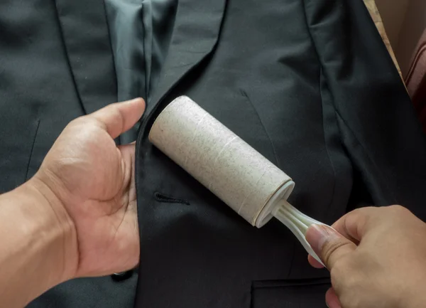 Dry cleaning and business theme: a man hand with black suit holding a white sticky brush for cleaning clothes and furniture from dust