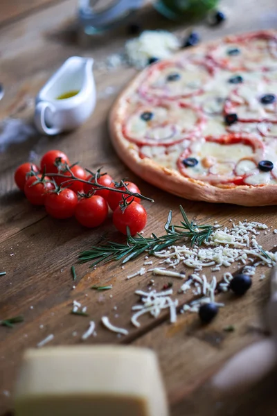 Different ingredients and circle pizza on table.