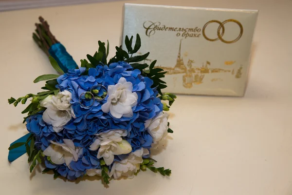 Two platinum wedding rings lie on a bouquet of blue and white flowers. The certificate of marriage.