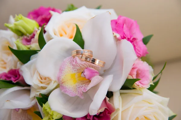 Two wedding gold rings with a diamond lying on the bride\'s bouquet of white orchids and pink flowers.