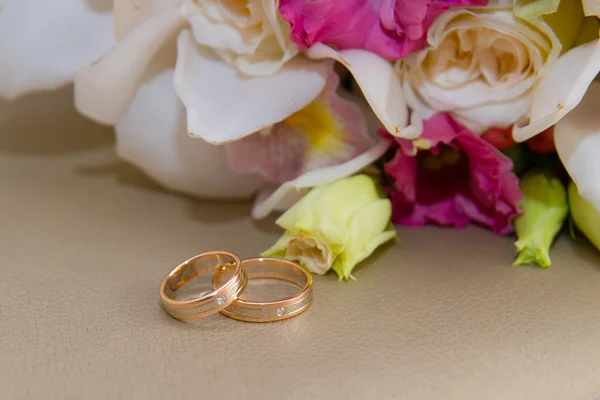 Two gold wedding rings with diamond lie around the bride\'s bouquet of white orchids and pink flowers.