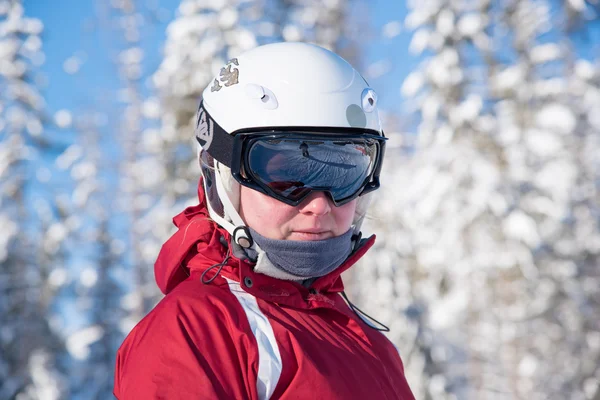 Young skiing woman wearing black goggles, white helmet and red jacket