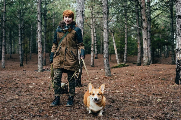 Redhead girl walking with welsh corgi dog in the forest