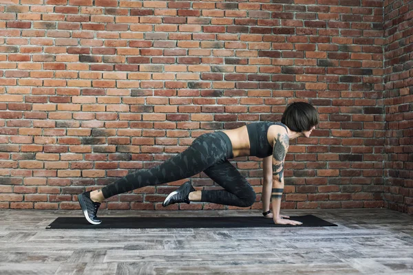 Tattooed female doing exercises indoors, sporty woman practicing yoga