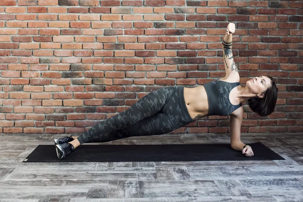 Tattooed female doing exercises indoors, sporty woman practicing yoga