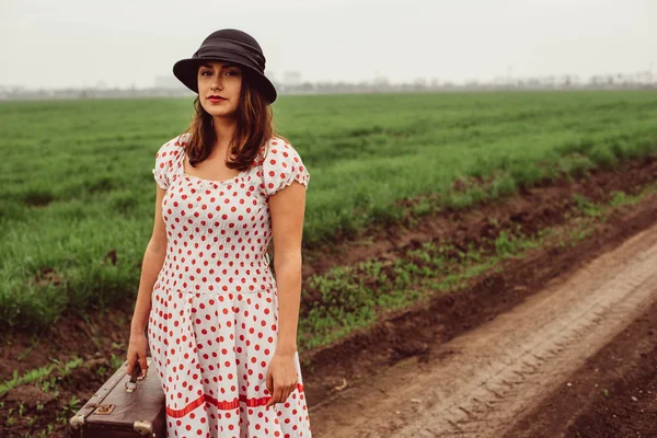 Woman in vintage clothes with suitcase in field.