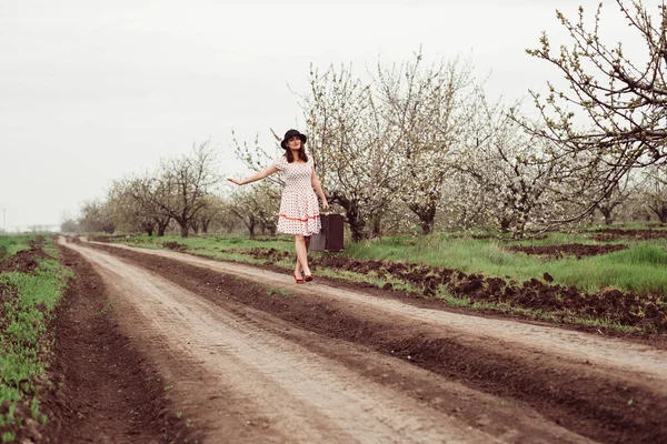 Woman in vintage clothes with suitcase in field.