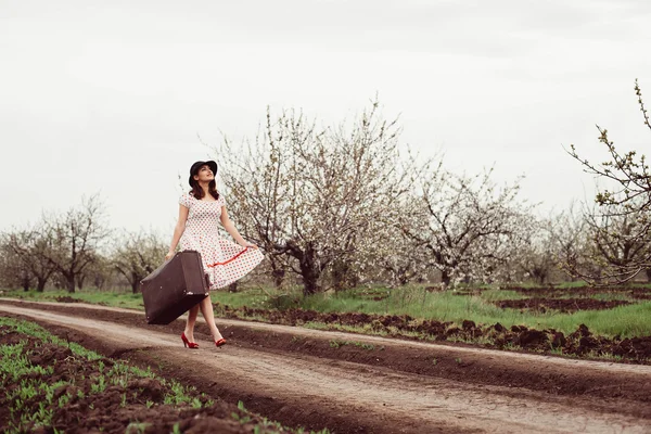 Woman in vintage clothes with suitcase in field.