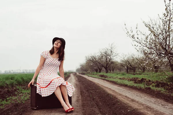 Woman in vintage clothes with suitcase in field.