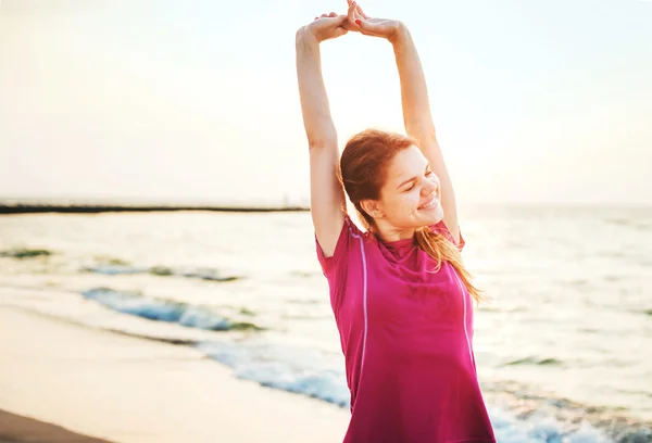 Fitness sport model smiling happy doing exercises during outdoor work out on sunrise. Beautiful caucasian female training outside on seaside in the morning