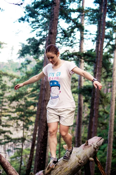 Caucasian hiker woman on trek in mountains living a healthy active lifestyle. Hiker girl on nature landscape hike in Crimea balancing on a tree, happy free female in the wood.