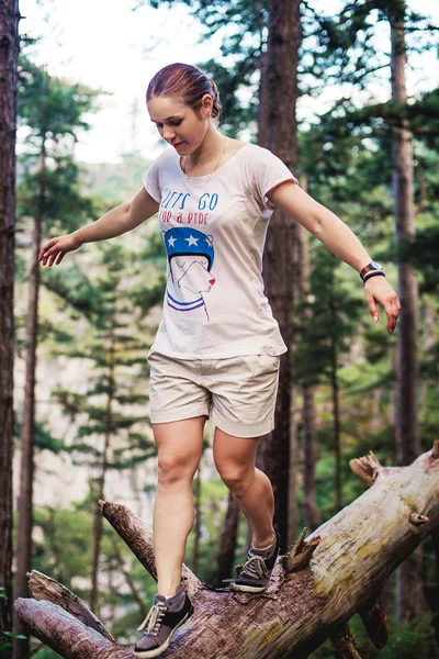 Caucasian hiker woman on trek in mountains living a healthy active lifestyle. Hiker girl on nature landscape hike in Crimea balancing on a tree, happy free female in the wood.