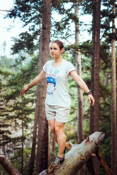 Caucasian hiker woman on trek in mountains living a healthy active lifestyle. Hiker girl on nature landscape hike in Crimea balancing on a tree, happy free female in the wood.