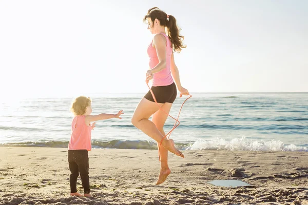 Family workout - mother and daughter doing exercises on beach.