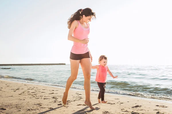 Family workout - mother and daughter doing exercises on beach.