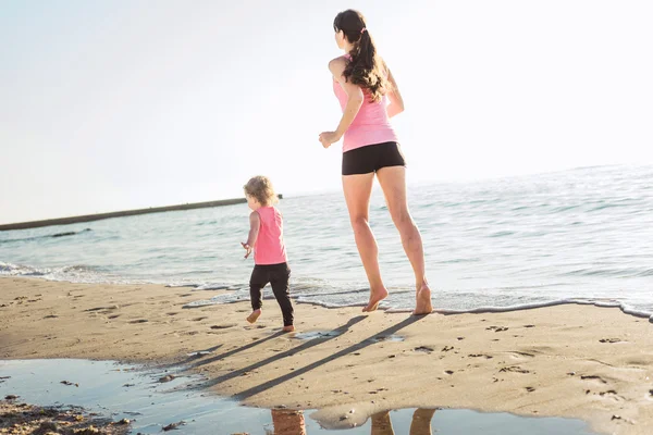 Family workout - mother and daughter doing exercises on beach.