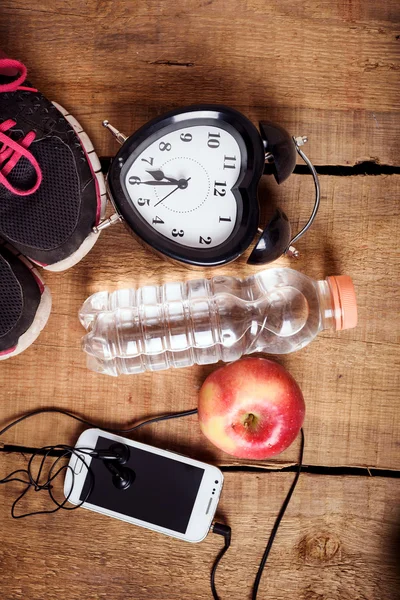 Sport equipment. Sneakers, water, apple, alarm clock, smartphone and earphones on wooden background. Clothes for running. Morning running concept