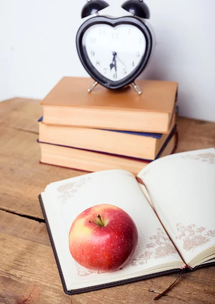 Books, alarm clock, notepad, cellphone with earphones and apple on wooden background. Education equipment, education concept