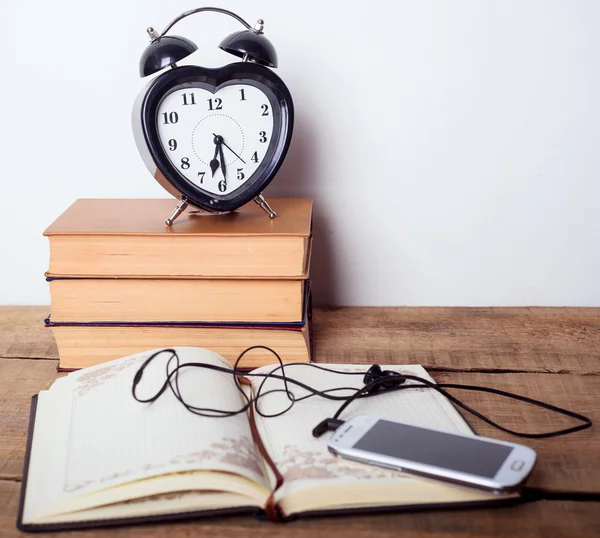Books, alarm clock, notepad, cellphone with earphones  on wooden background. Education equipment, education concept
