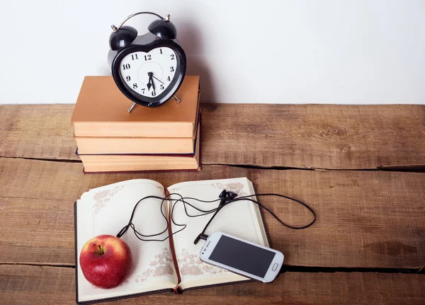 Books, alarm clock, notepad, cellphone with earphones and apple on wooden background. Education equipment, education concept
