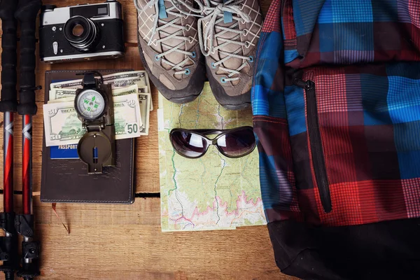 Travel equipment - hiking boots, map, backpack, trekking poles, vintage camera, sunglasses, compass, cellphone, earphones, notebook, pen, apple, passport and money