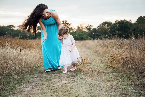 Mother and daughter playing on autumn field together, loving family having fun outdoors