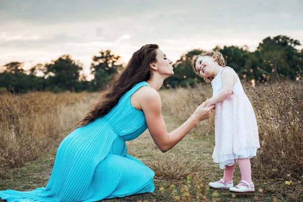 Mother and daughter playing on autumn field together, loving family having fun outdoors