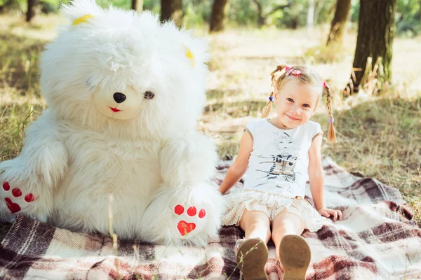 Little pretty girl playing with large white bear toy in park
