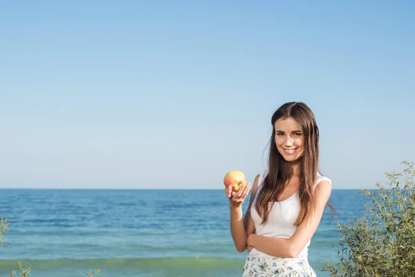 Young caucasian female on seaside with apple. Girl eating apple, healthy eating and healthy living concept