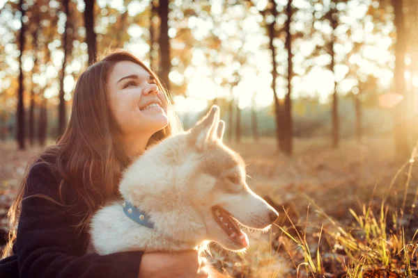 Young happy female having fun with siberian husky dog in autumn park during sunset