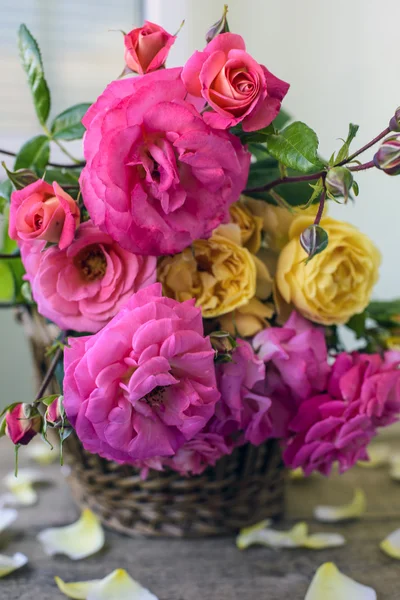 Bouquet of pink and yellow roses in a wicker basket and white sheet of paper for a message
