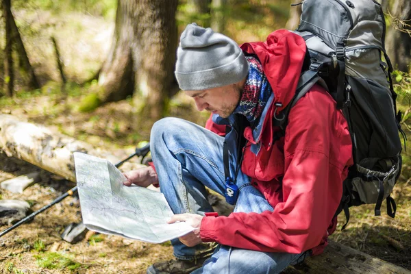 Young caucasian male with a map in the forest, hiker looking at map outdoors