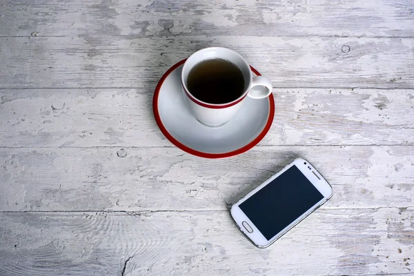 Cup of tea and mobile phone on white wooden background