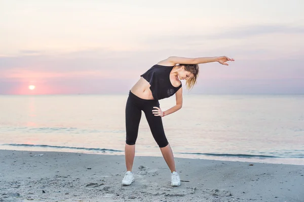 Fitness sport model smiling happy doing exercises during outdoor work out on sunrise. Beautiful caucasian female training outside on seaside in the morning