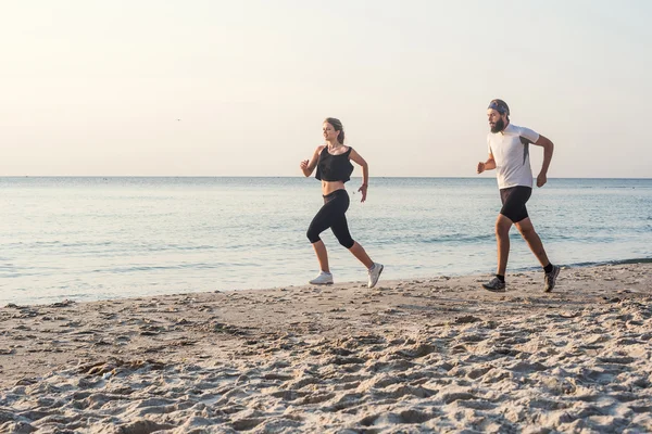 Running people - woman and man athlete runners jogging on beach. Fit young fitness couple exercising healthy lifestyle outdoors during sunrise or sunset