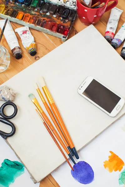 Watercolor paints,oil paints, cellphone, glasses and brushes on the table in the artist\'s studio.