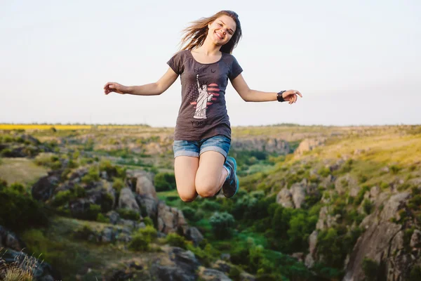 Young caucasian female jumping in canyon, girl having fun on beautiful natural landscape with rocks