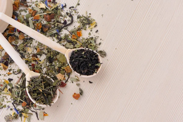 Assortment of dry tea in spoons, on wooden background