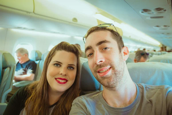 Happy couple taking selfie with smartphone or camera inside airplane