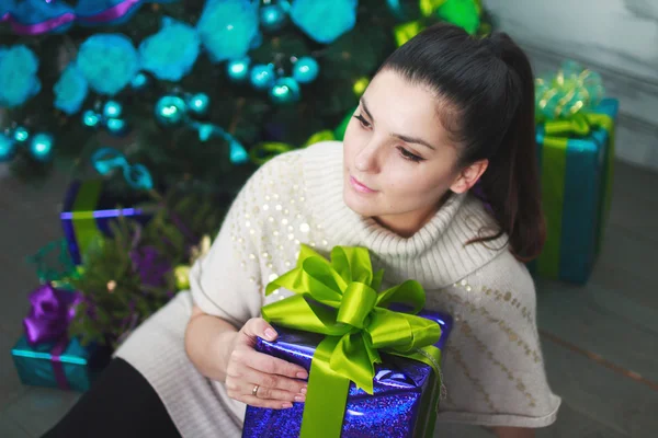 Girl sits near a Christmas tree with gifts