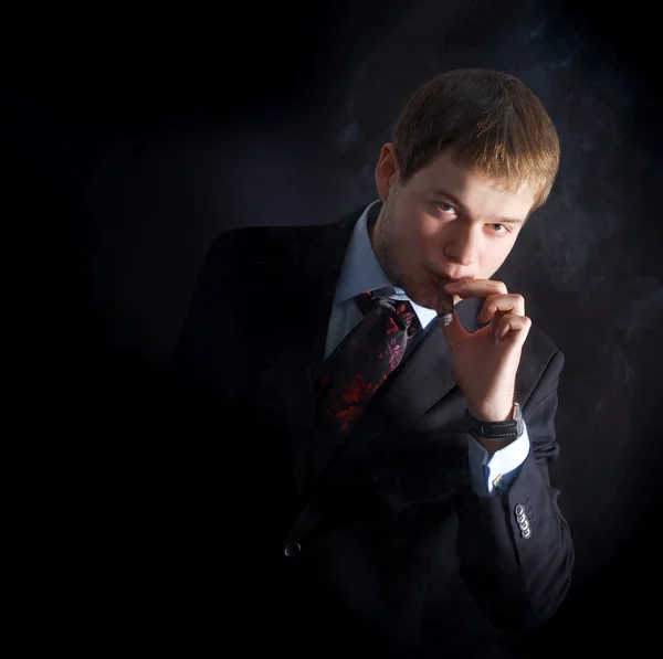 The man smoke a cigar with lots of smoke. A dark background