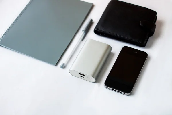 Objects on white table (phone, purse, notebook, pen, portable charging)