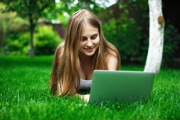 Beautiful girl working at a laptop lying on green grass