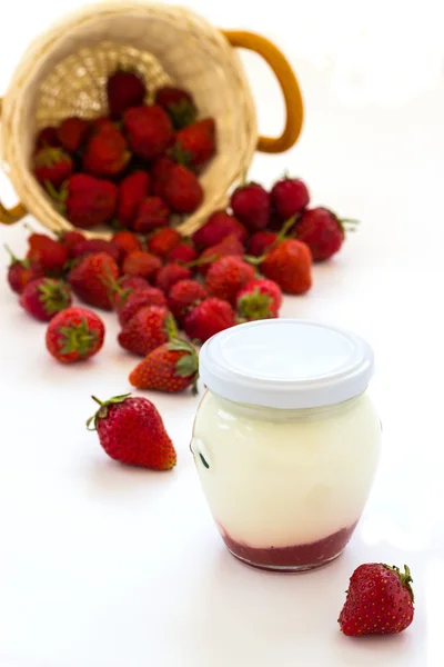 Strawberry yoghurt in a glass jar and basket of strawberries on white background