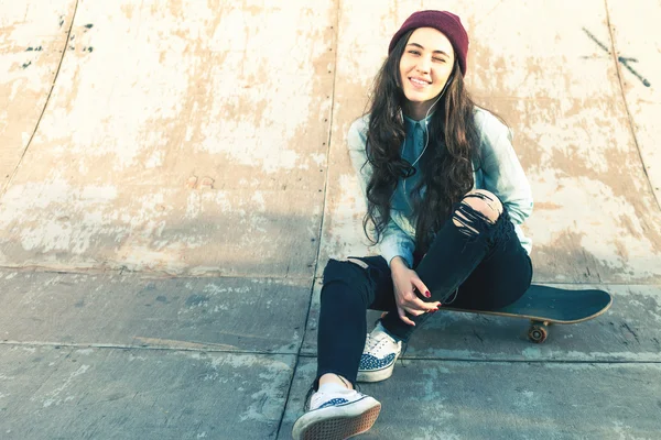 Happy skateboarder girl with skateboard outdoor sitting at skatepark