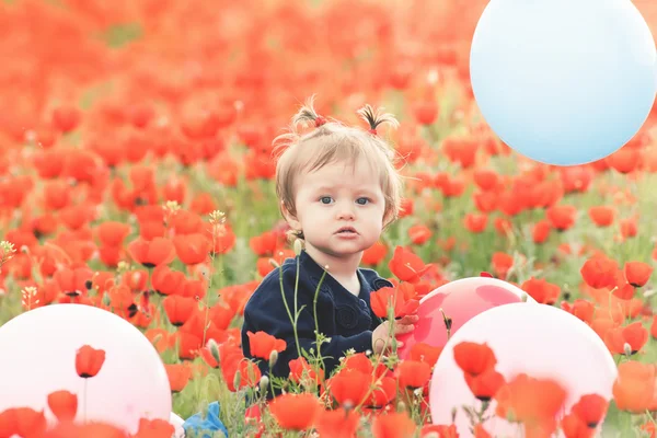 Funny child holding a balloon outdoor at poppy field
