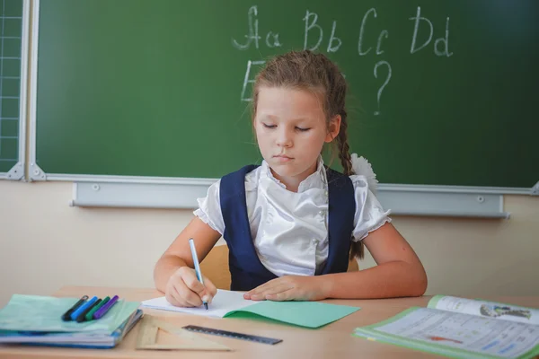 Schoolgirl sitting at desk at school and writing to notebook
