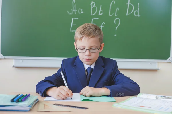 Schoolboy sitting at desk at school and writing to notebook