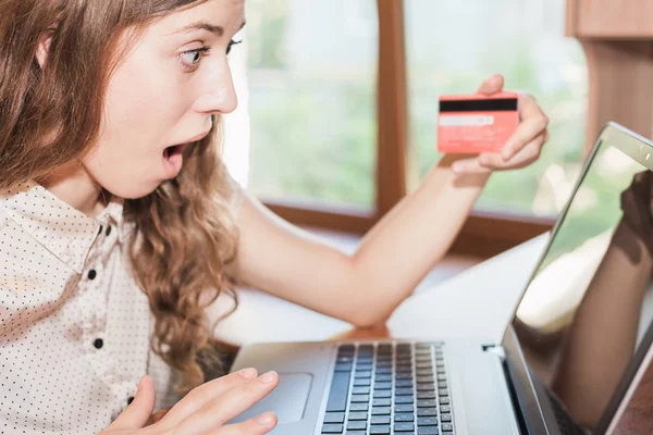 Beautiful surprised woman holding credit card, and shopping through laptop